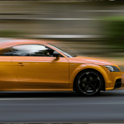Orange sports car driving at high speed on road.