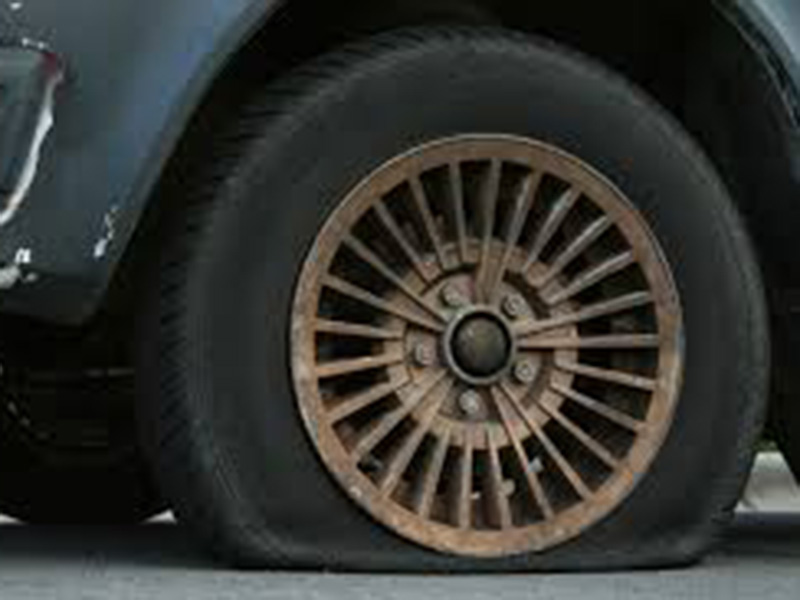 A flat car tire with an old, spoked wheel resting on the ground.