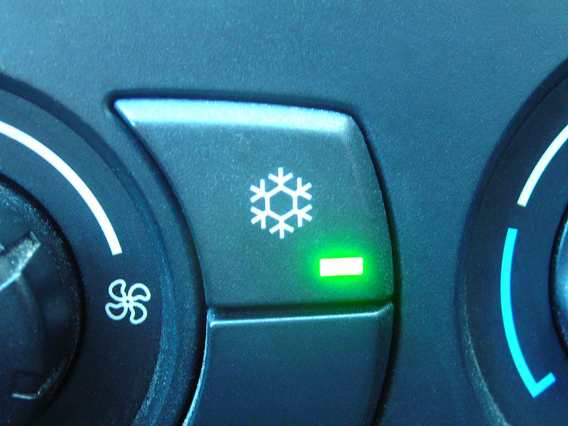 A car dashboard showing the air‑conditioning button with a snowflake symbol.
