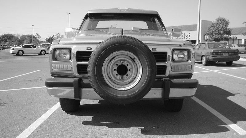 Front view of a Dodge pickup truck with a spare tire mounted on the grille in a parking lot.