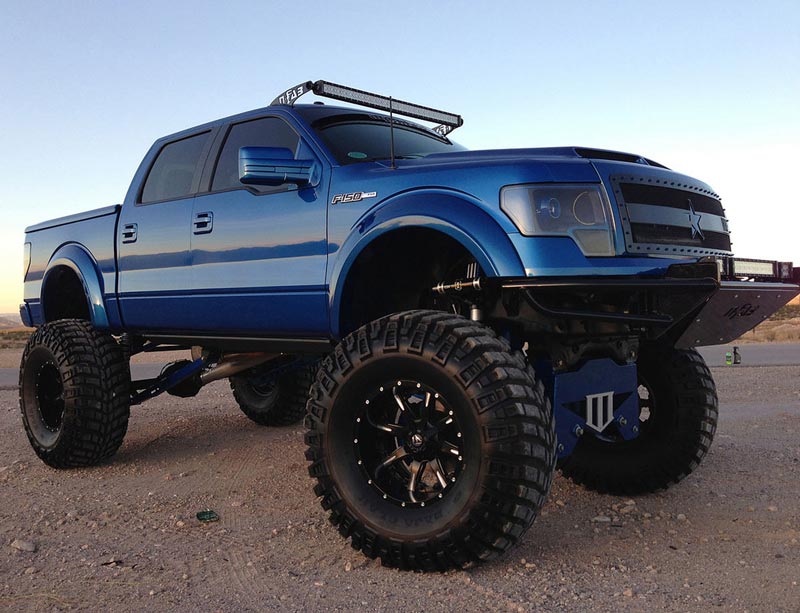 A lifted blue pickup truck with oversized off-road tires
