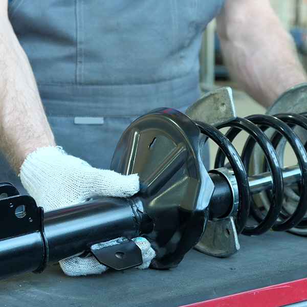 An auto mechanic prepares a new shock absorber rack for installation during repair and maintenance of the car