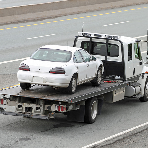 Rear quarter view of a tilt bed tow truck on a highway carrying a nondescript vehicle