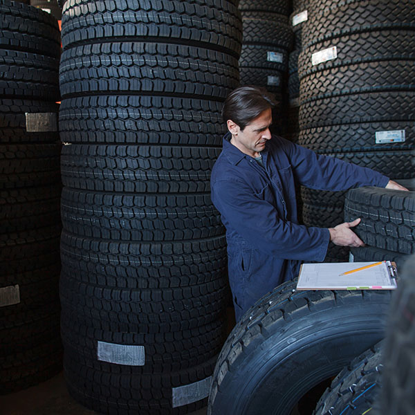 Mechanic lifting new car tire from stack of tires inventory to make a vehicle repair
