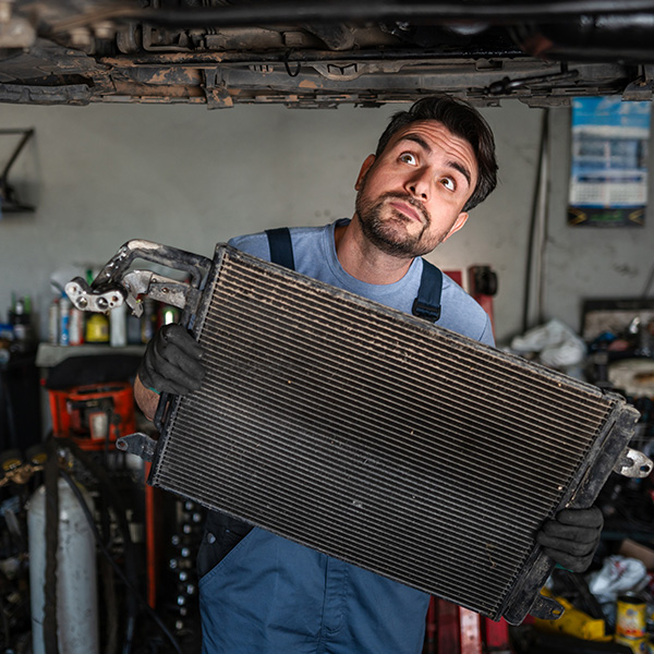Auto mechanic holding radiator and looking up at vehicle in garage