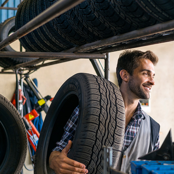 Smiling mechanic carrying tire at auto repair shop