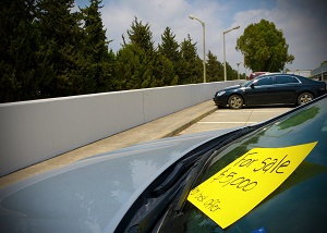 Car windshield with a yellow “For Sale” sign showing price.