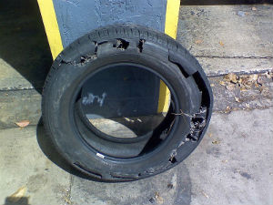 Severely damaged car tire with large tears leaning against a wall.